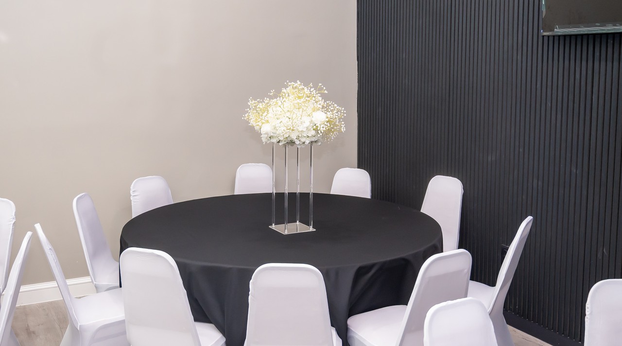 Round reception table with black linen, white chairs, and a tall white floral centerpiece against the black slatted feature wall