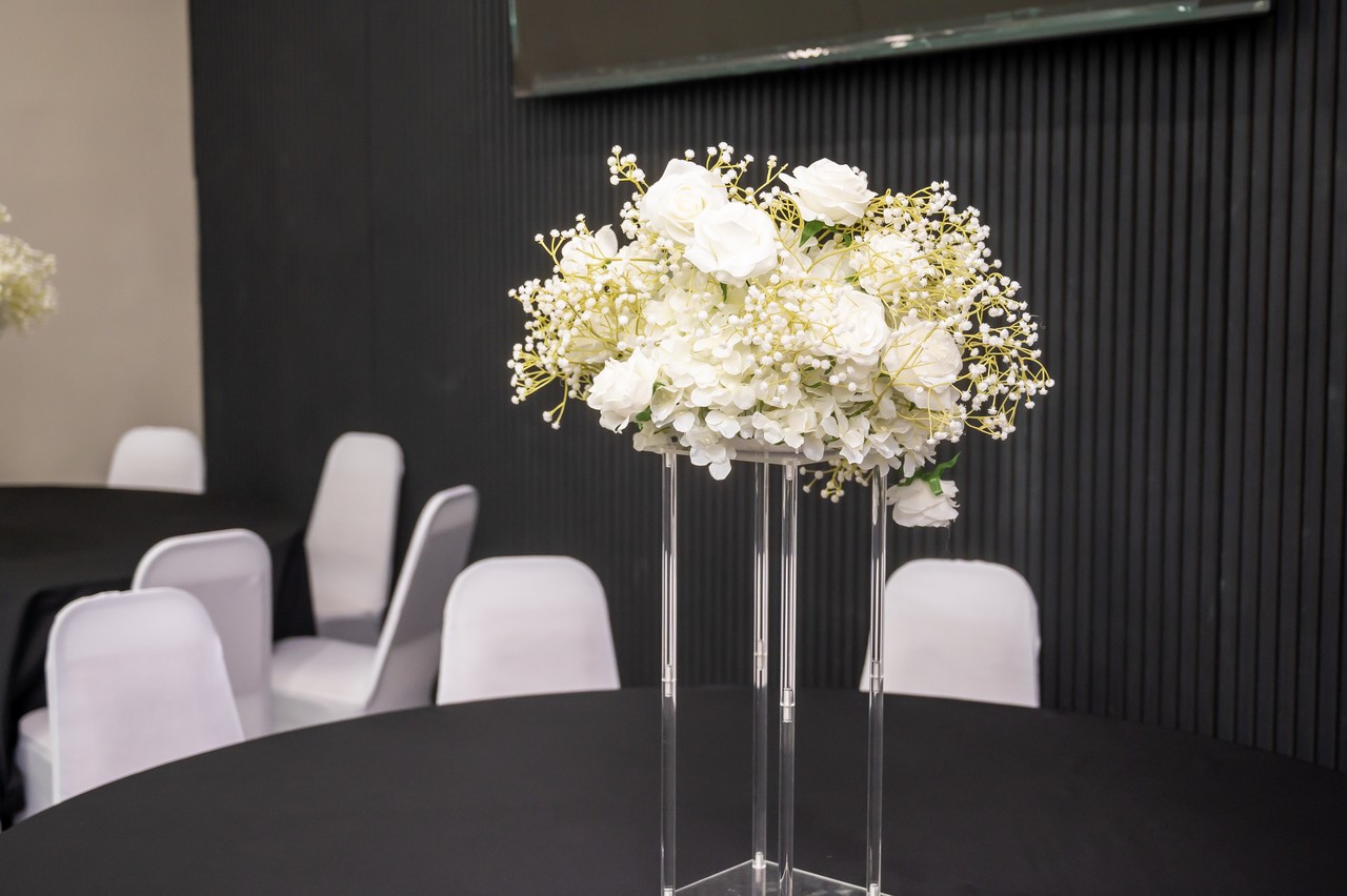 White floral centerpiece on a clear stand above a black tablecloth against the slatted feature wall