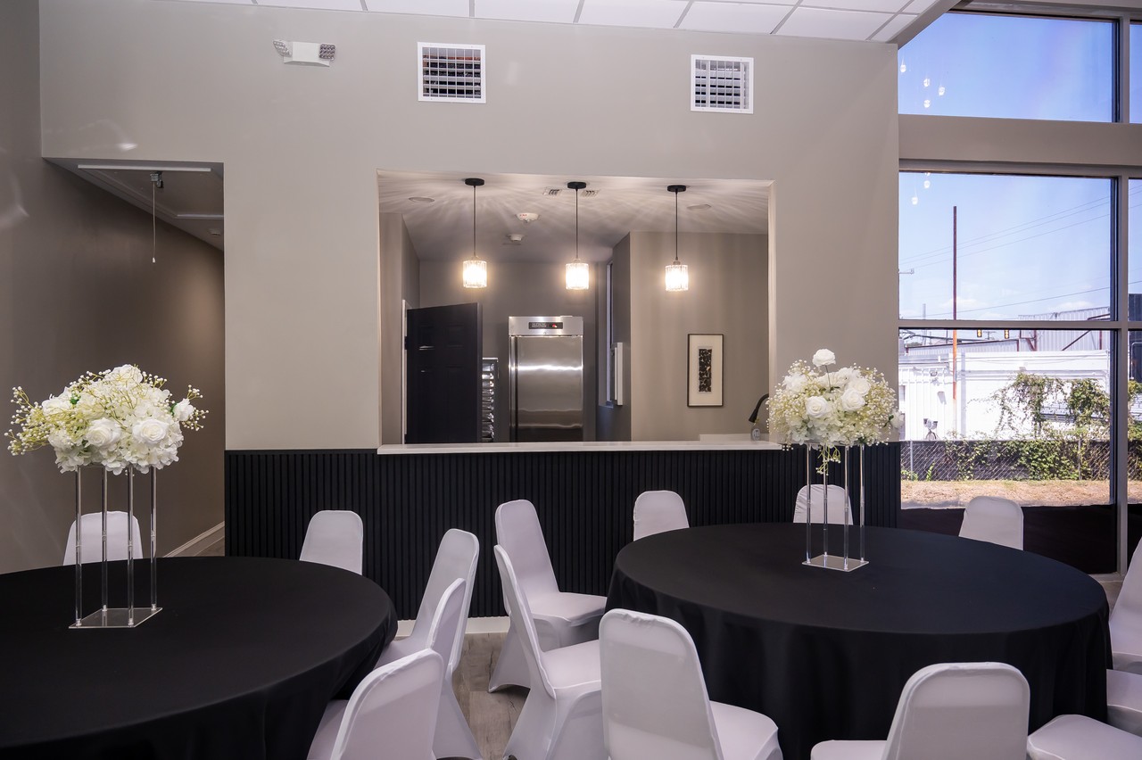 Kitchen pass-through with pendant lights beside decorated tables, black linens, and white floral centerpieces
