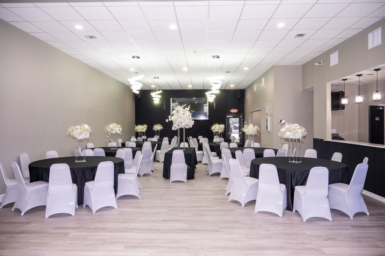 Decorated main hall facing the black feature wall, with black linens, white chairs, tall florals, and spiral chandeliers