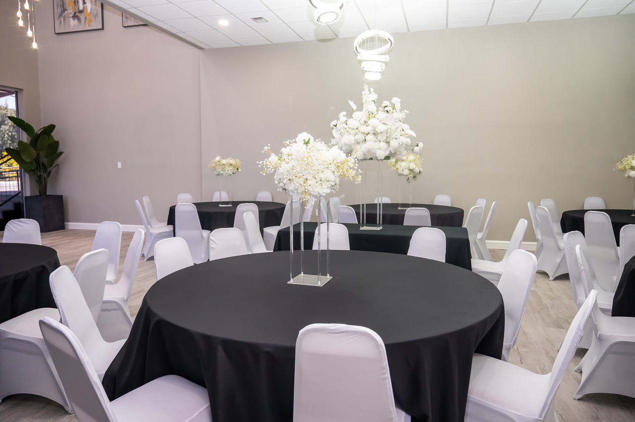Decorated reception tables with black linens, white chairs, and tall floral centerpieces across the hall