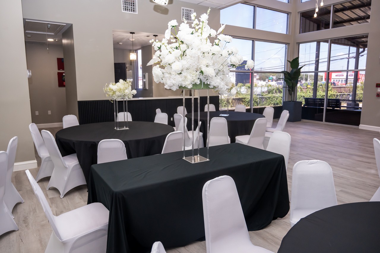 Decorated reception tables beside floor-to-ceiling windows with black linens and tall white florals